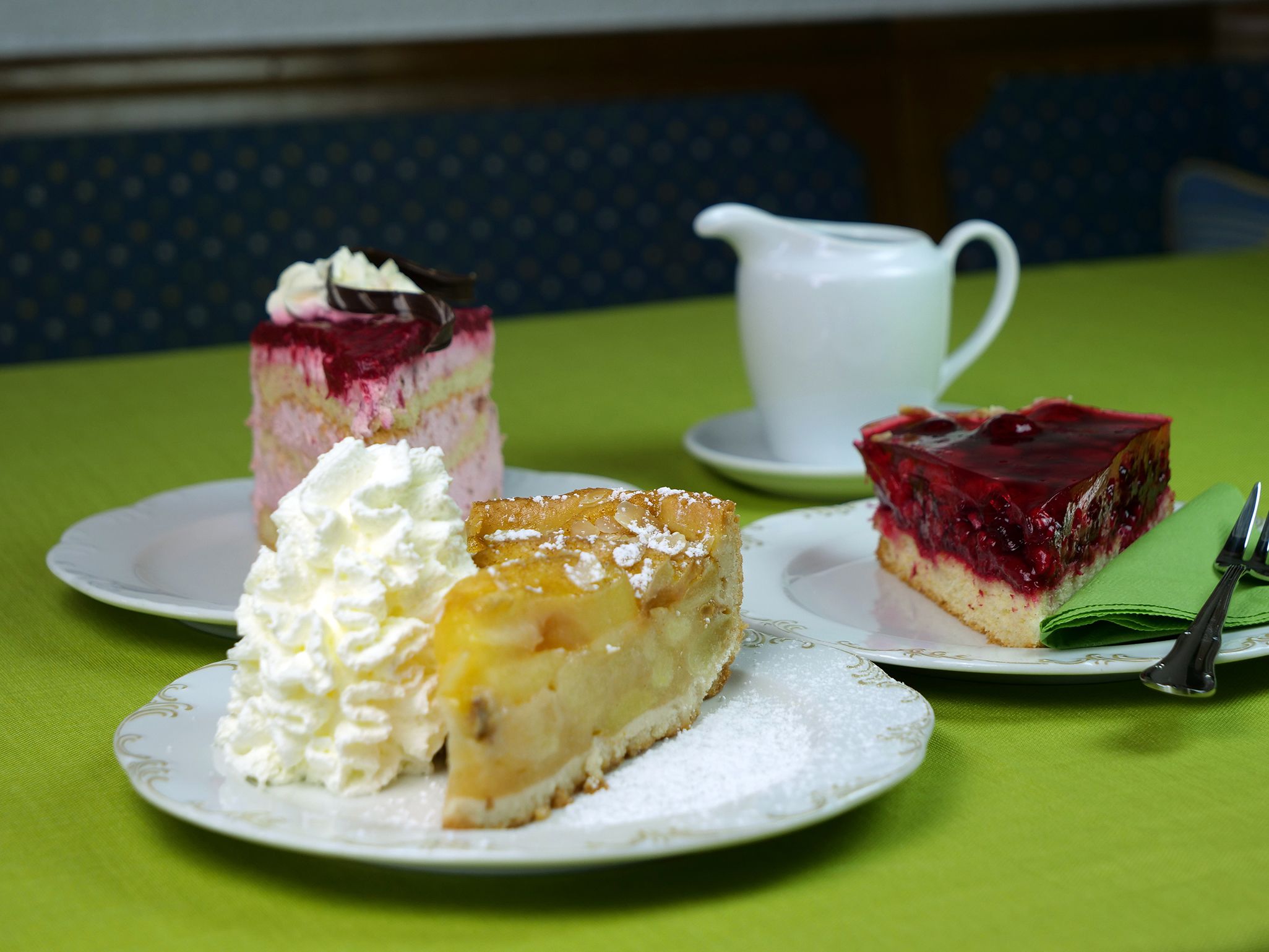 A table with three plates of desserts, a white pitcher, and a green tablecloth.