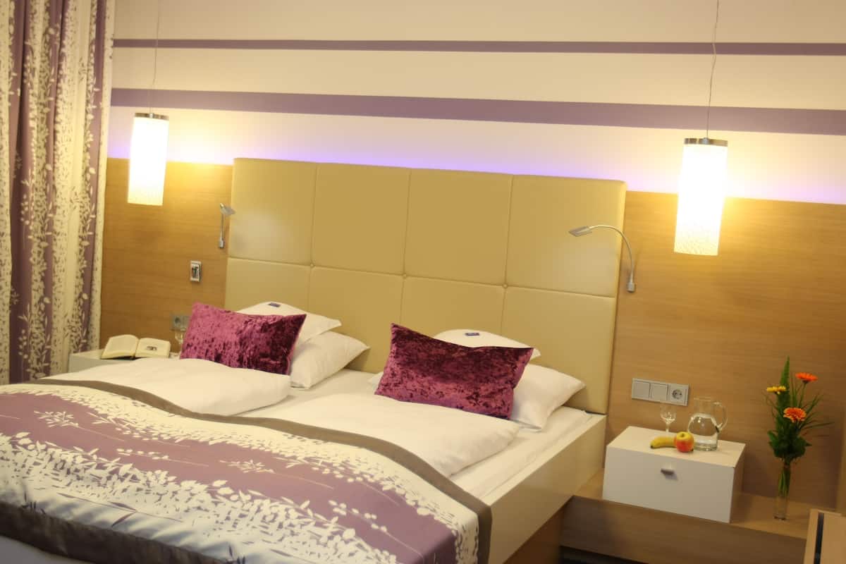 Une chambre d’hôtel avec un grand lit, deux tables de chevet, une petite table et une lampe fixée au mur.