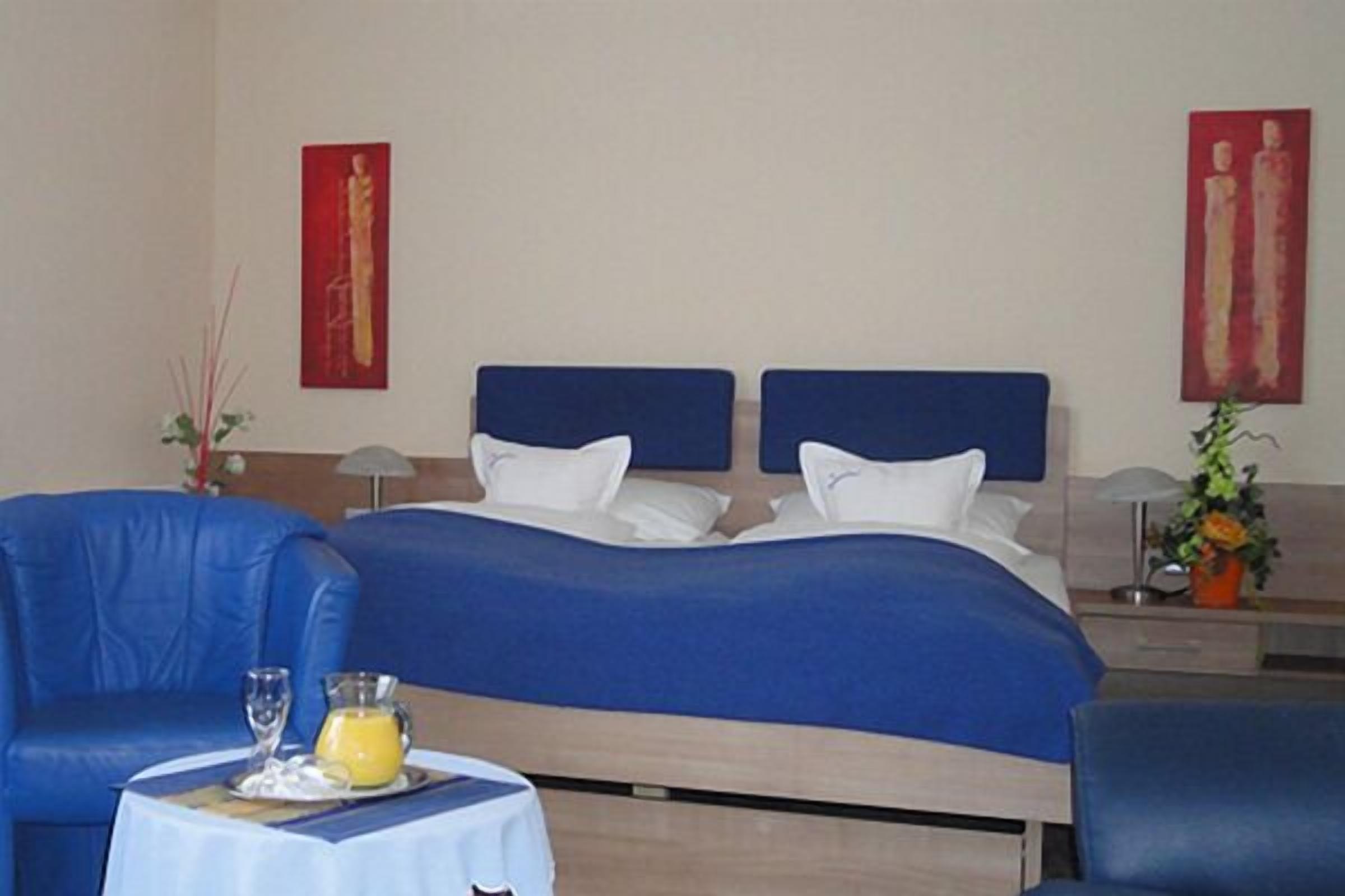 Habitación de hotel con una cama doble, dos sillones azules, una mesita con una bandeja de desayuno y dos cuadros rojos en las paredes.