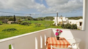 A balcony with a table and chairs, overlooking a green landscape and white buildings. - Nikos 2 Studios & Apartments (Kos)