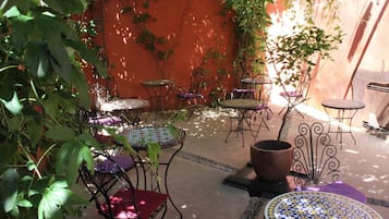 An outdoor patio with several round tables and chairs, surrounded by potted plants and a red wall.