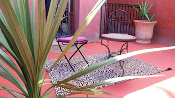 Un patio con un alfombra estampada, una planta en maceta, una silla de metal y una mesa.