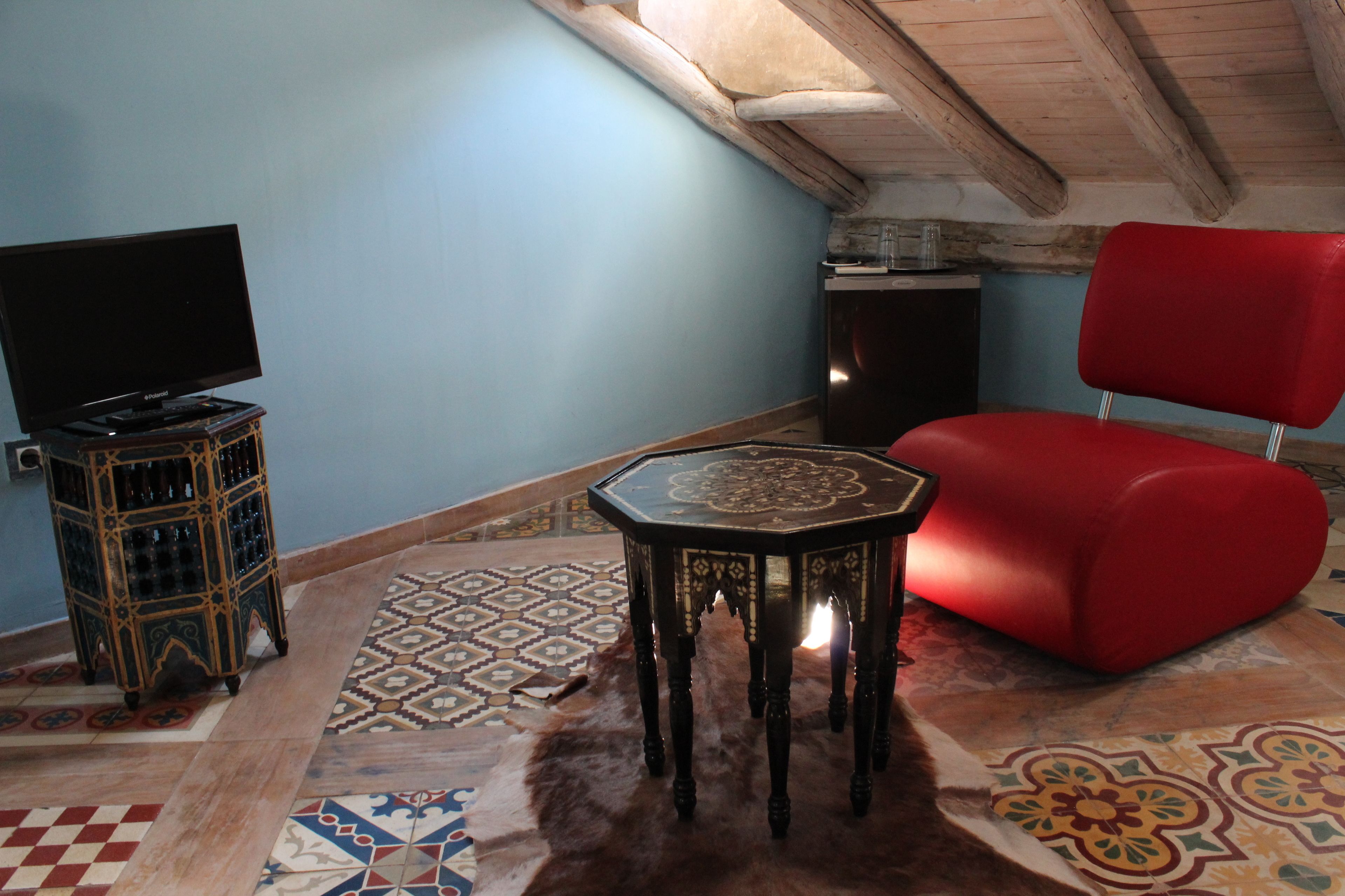 Una habitación con una televisión sobre un mueble bajo, una silla roja y una alfombra estampada en el suelo.
