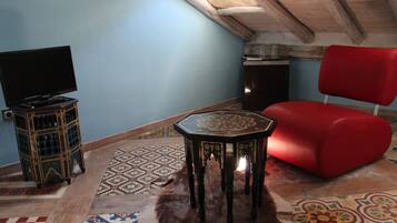 Una habitación con una televisión sobre un mueble bajo, una silla roja y una alfombra estampada en el suelo.