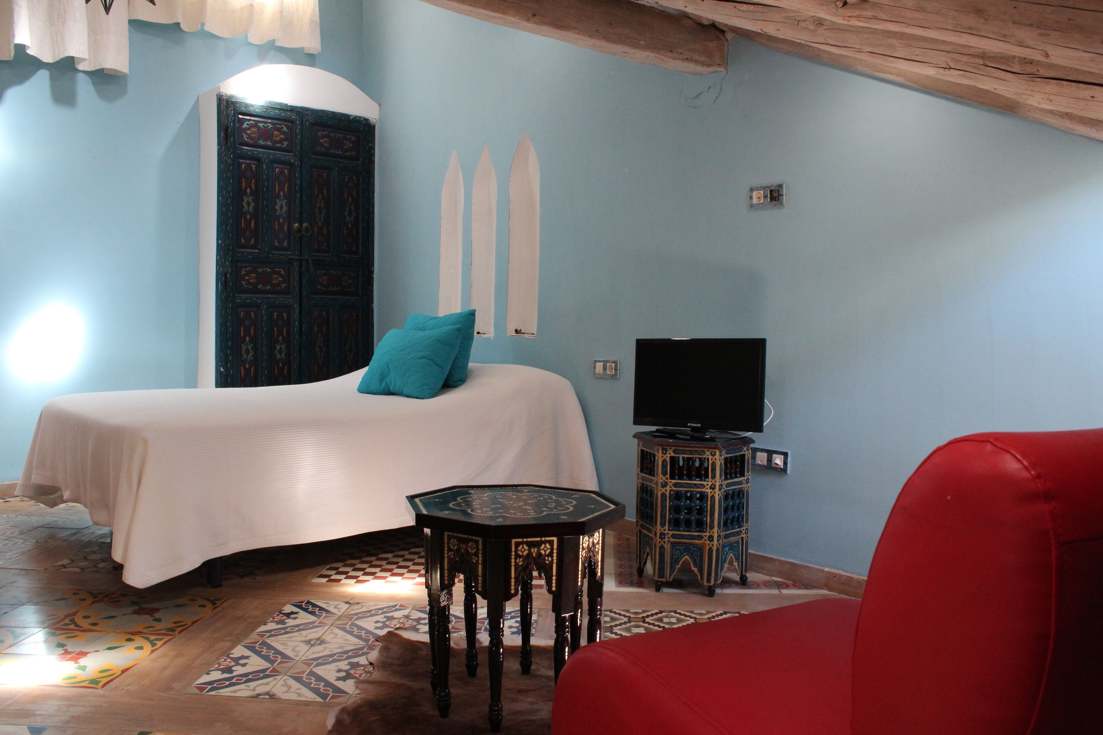 A bedroom with a bed, a red chair, a television, and a decorative cabinet.