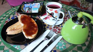 Una mesa con tostadas, una taza de té, un calentador de tetera y una bandeja con productos envasados.