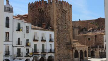 Una torre de piedra histórica con almenas, junto a edificios blancos con balcones y letreros que indican 'King Kebab'.