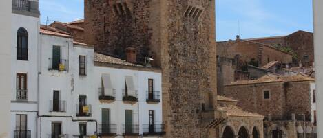 Una torre de piedra histórica con almenas, junto a edificios blancos con balcones y letreros que indican 'King Kebab'.