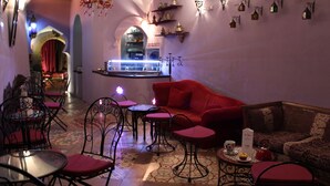 Un interior acogedor con un sofá rojo, varias mesas y sillas, una zona de bar y apliques decorativos en la pared.