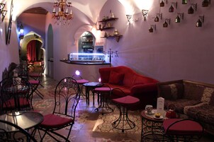 Un interior acogedor con un sofá rojo, varias mesas y sillas, una zona de bar y apliques decorativos en la pared.
