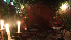Un patio al aire libre con mesas y sillas, rodeado de follaje e iluminado por velas.