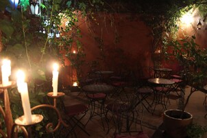 Un patio al aire libre con mesas y sillas, rodeado de follaje e iluminado por velas.