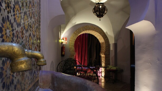 Un pasillo estrecho con un muro de azulejos, un arco de ladrillo y una cortina roja.