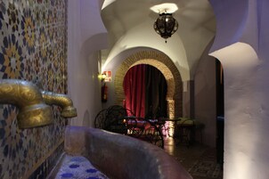 Un pasillo estrecho con un muro de azulejos, un arco de ladrillo y una cortina roja.