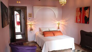 A bedroom with a bed, two bedside lamps, a chair, a door, and a wall with artwork.