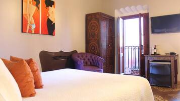 Una habitación de hotel con una cama grande, un sillón morado, un armario de madera y un televisor en la pared.