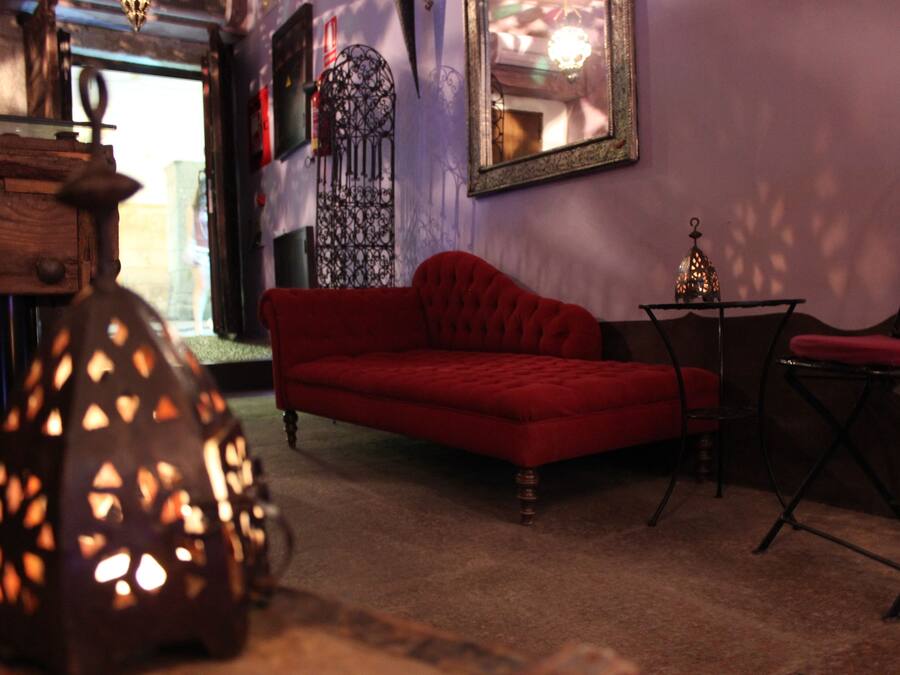 Una habitación con un sofá rojo, una pequeña mesa con una lámpara y un portón metálico decorativo.