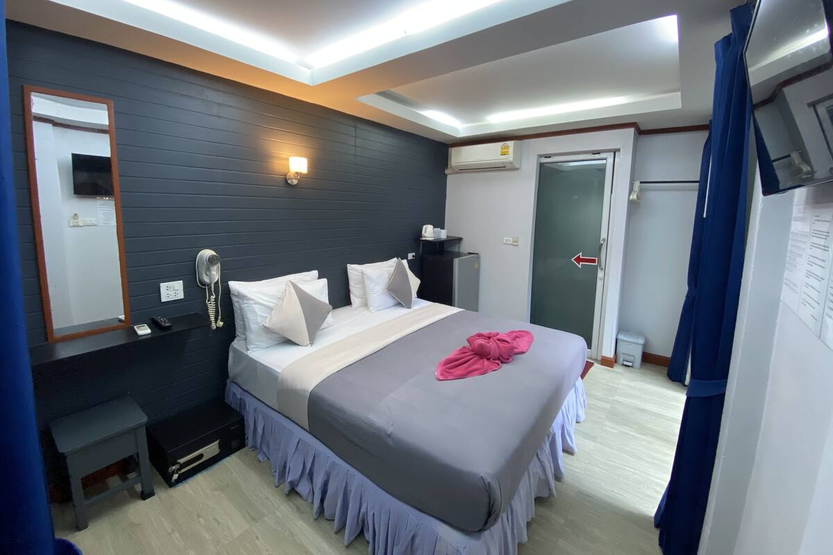 A modern hotel room with a bed, bedside table, mirror, and an air conditioning unit.