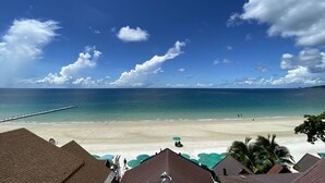 A beach view with a clear sky, a wooden pier extending into the sea, and a row of buildings with green umbrellas. - Sinsamut Koh Samed Hotel (Rayong)