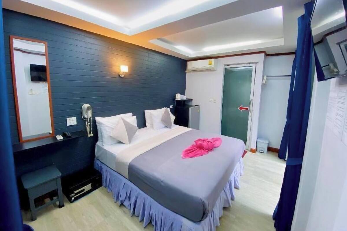 A hotel room with a bed, bedside table, mirror, wall-mounted TV, and a door with an arrow sign.