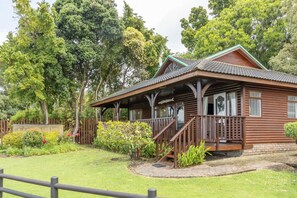A wooden cabin with a porch, surrounded by lush greenery and trees.