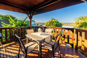 A wooden deck with a table and chairs, overlooking a lake and greenery.