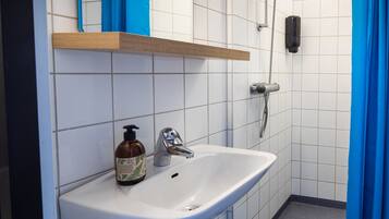 A bathroom with a white sink, a soap dispenser, and a shower head.