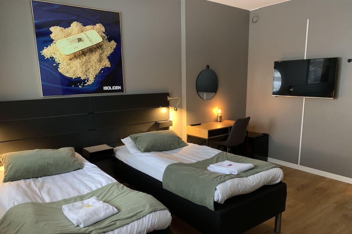 A hotel room with two beds, a desk, a chair, a TV, and a poster on the wall.