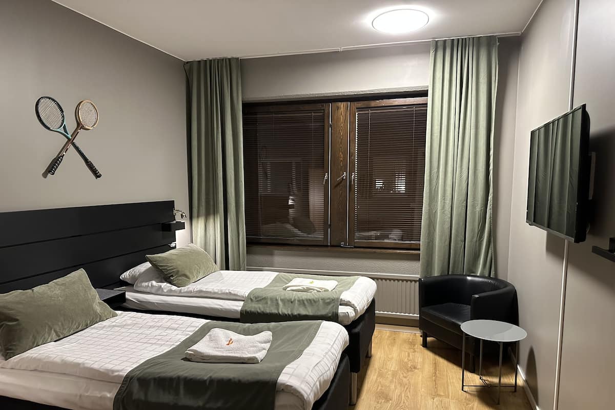 A hotel room with two beds, a TV, a small table, and a window with curtains.