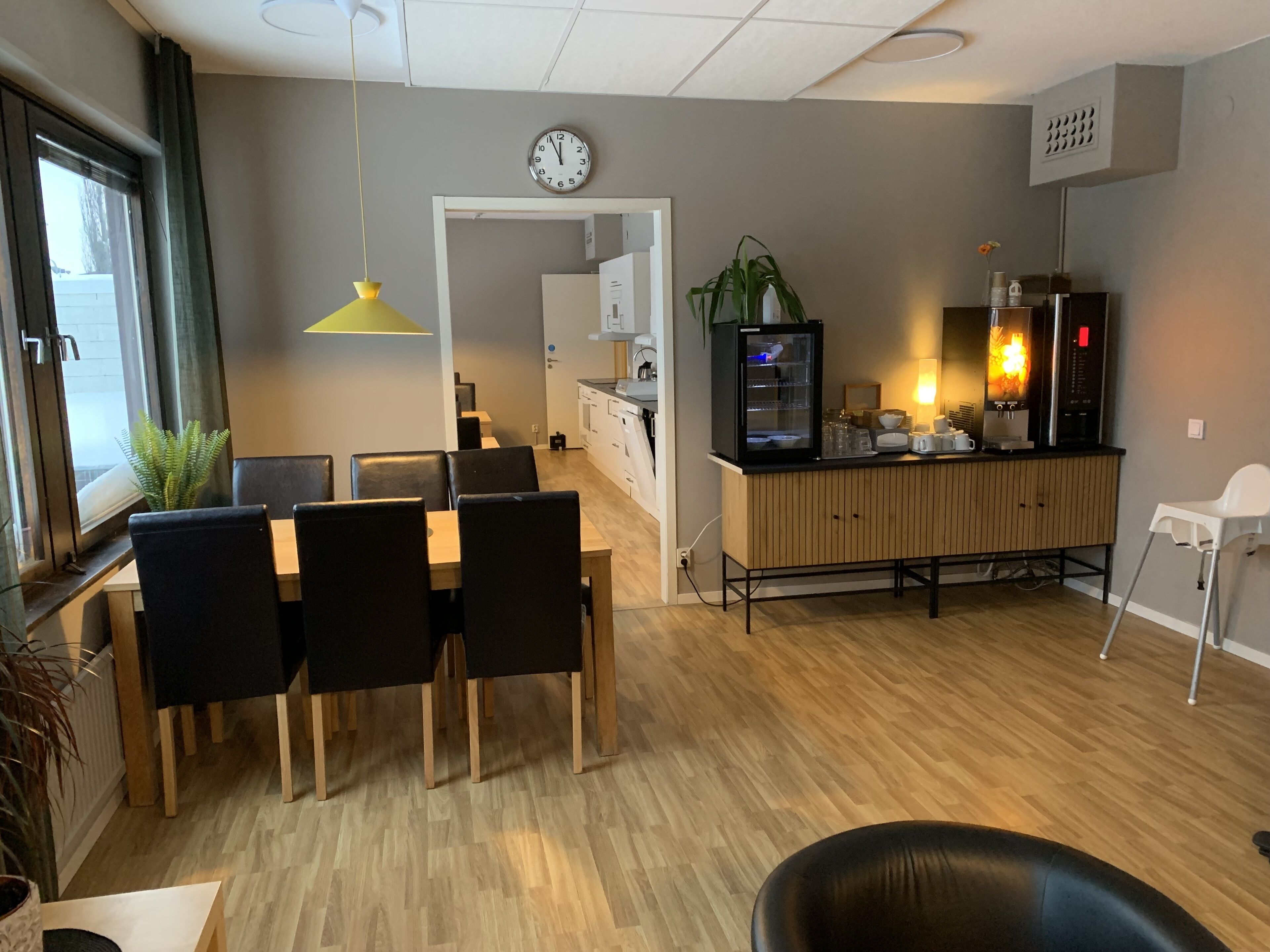 Une cuisine moderne équipée d’un réfrigérateur, d’un four à micro-ondes et d’une machine à café. On y trouve également un coin repas avec une table et des chaises, ainsi qu’une plante sur le rebord de la fenêtre.