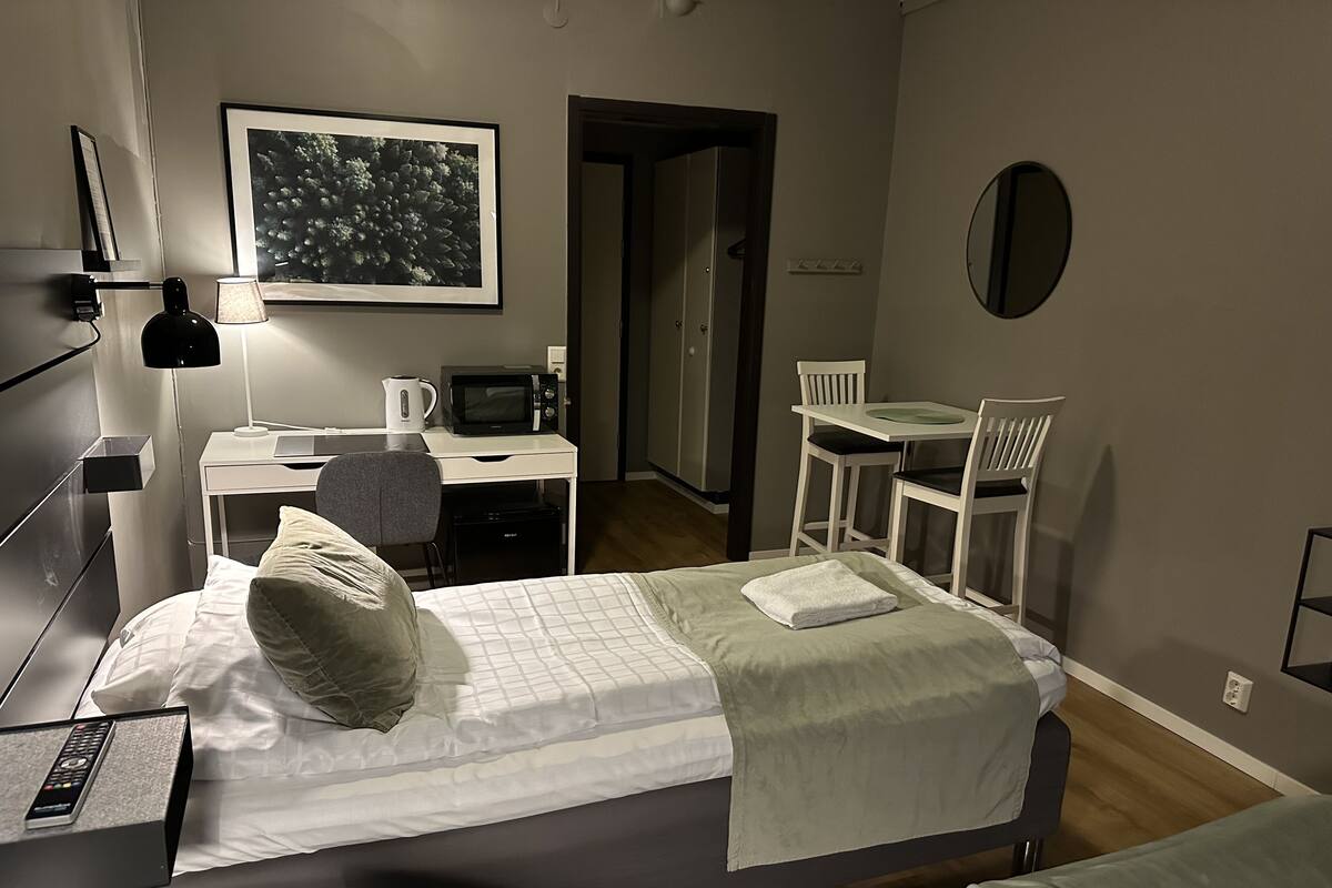 A hotel room with two beds, a desk with a computer, a chair, a small table, and a microwave.