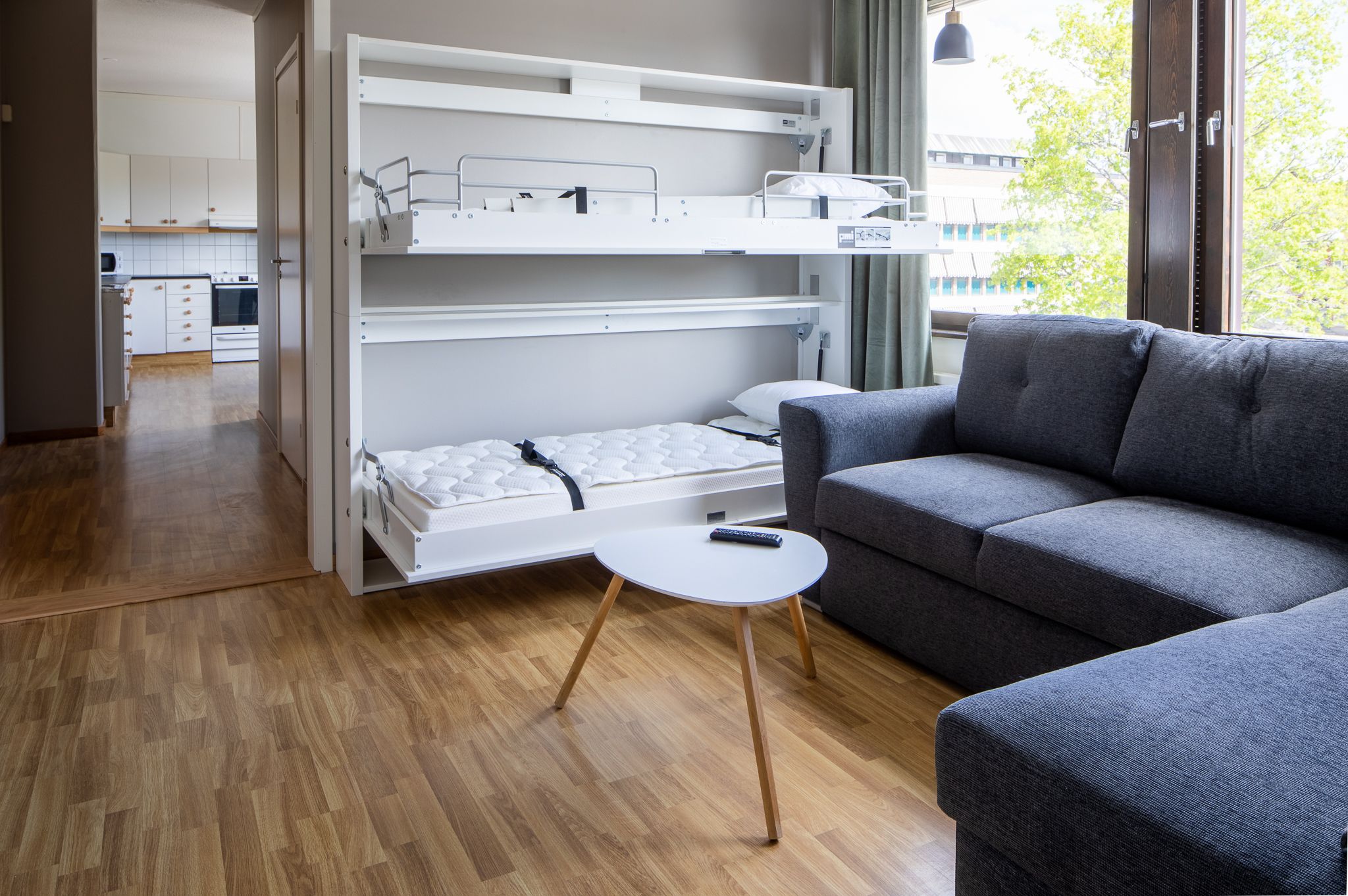 Een kleine kamer met een stapelbed, een grijze slaapbank en een witte tafeltje.
