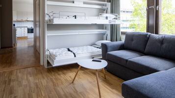Een kleine kamer met een stapelbed, een grijze slaapbank en een witte tafeltje.