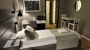 Una habitación de hotel moderna con cama, escritorio, silla y una pequeña cocina.
