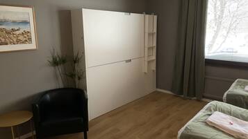 Ein Zimmer mit einem großen weißen Kleiderschrank, einem schwarzen Sessel, einem kleinen Tisch und zwei Betten mit grüner Bettwäsche.
