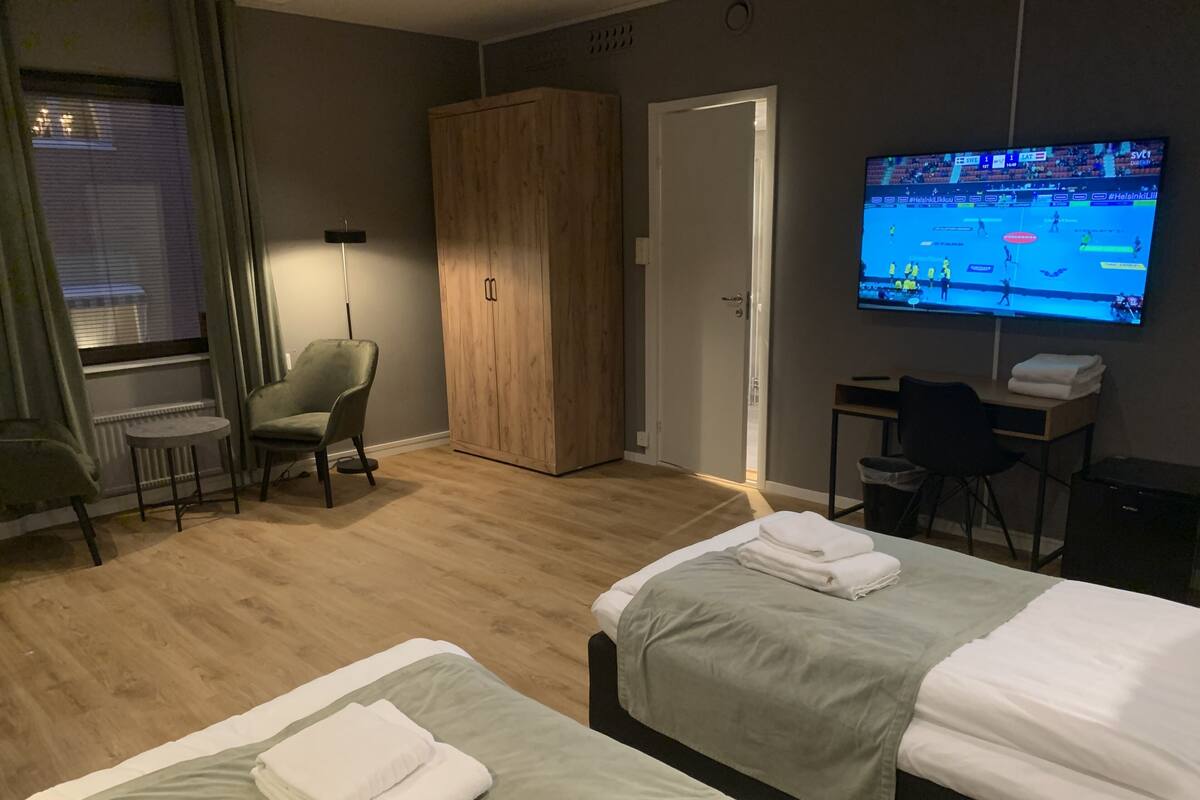 A hotel room with two beds, a desk, a chair, a wardrobe, a TV, and a window with curtains.