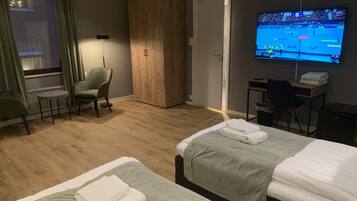 Habitación de hotel con dos camas, un escritorio, una silla, un armario, un televisor y una ventana con cortinas.