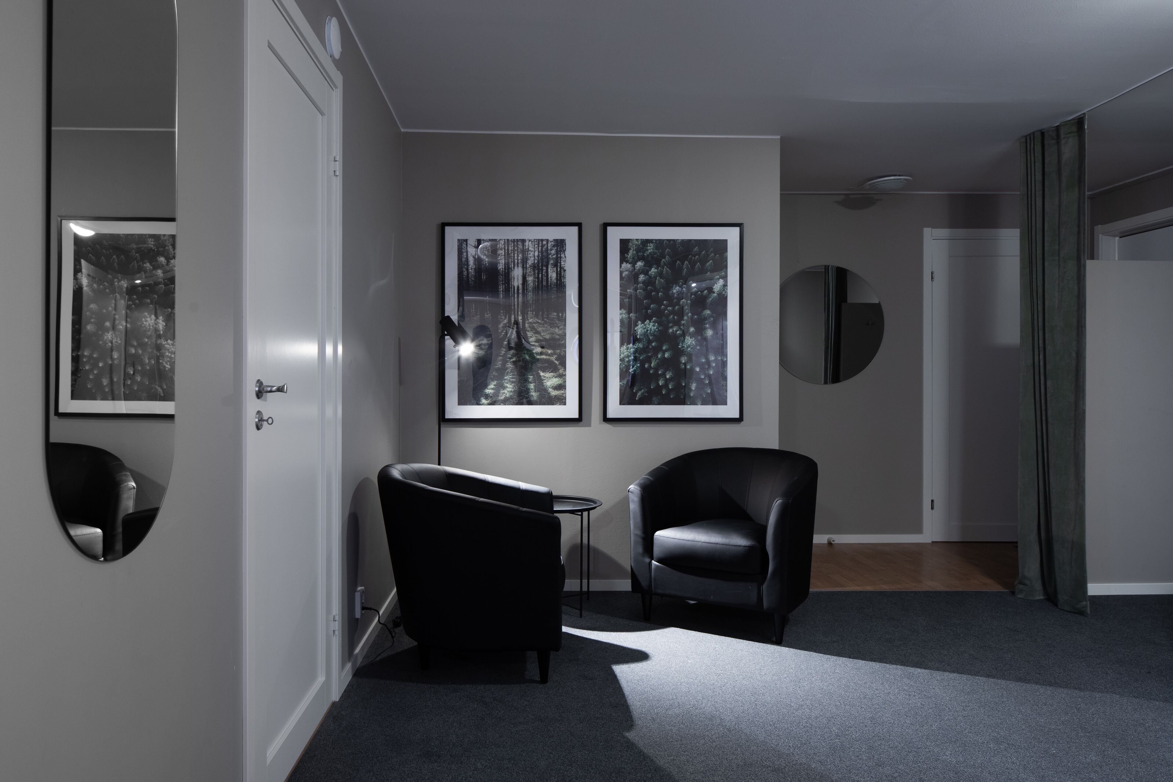 A modern living room with a dark leather sofa, a small round table, and two framed photographs on the wall.