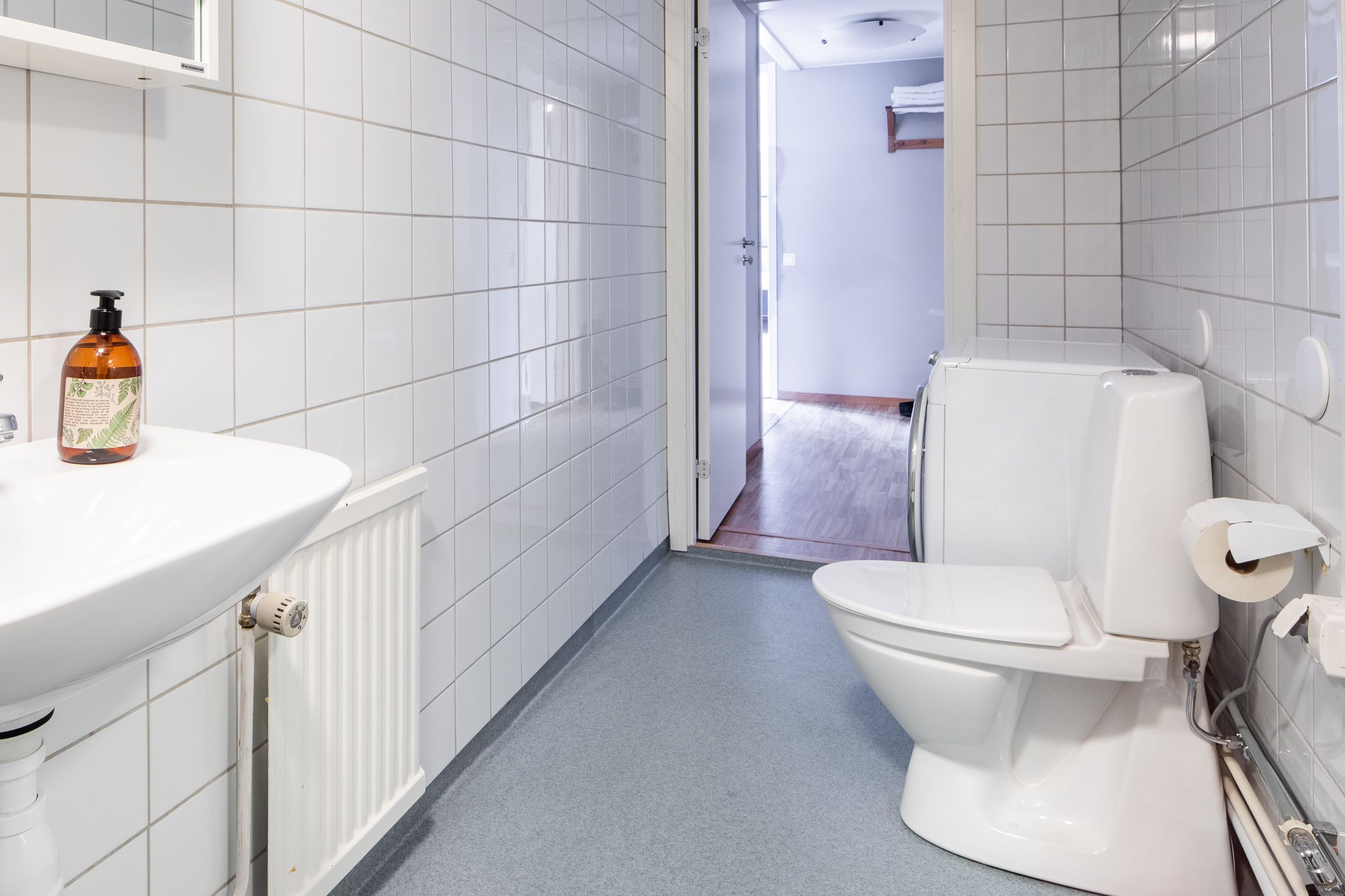 Une salle de bain avec des murs carrelés de blanc, un lavabo blanc, des toilettes et un espace douche.