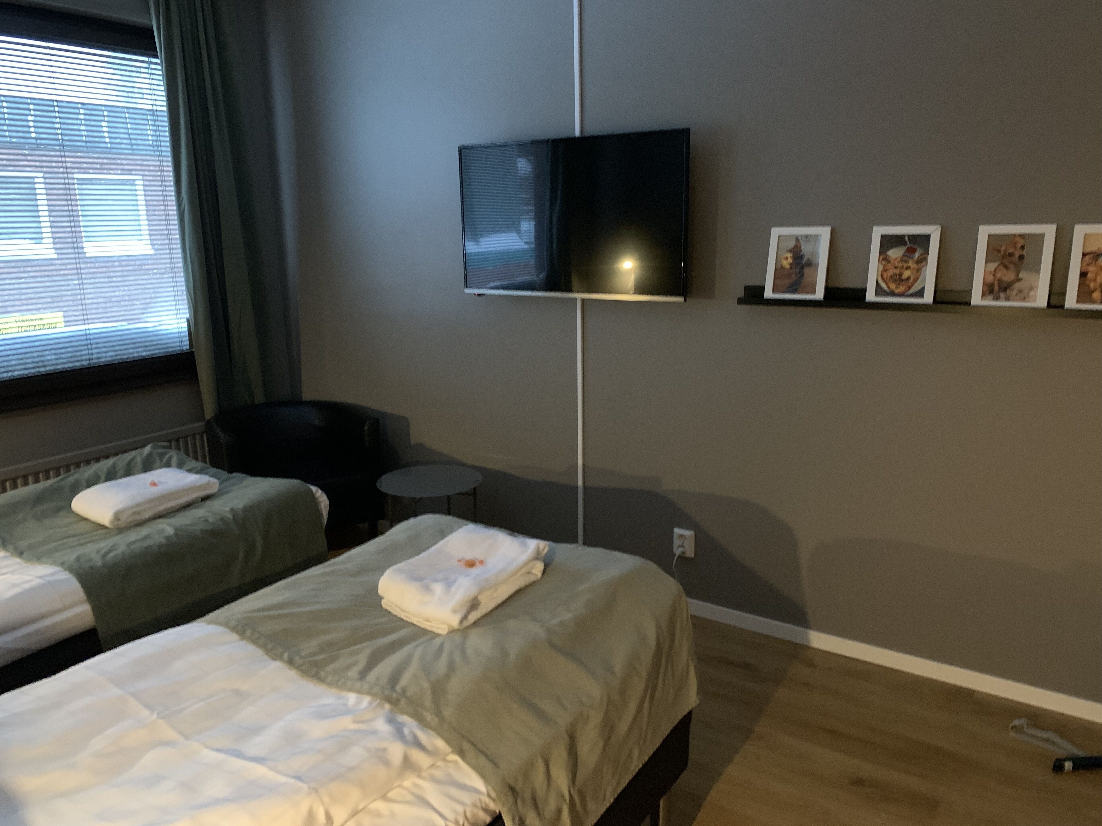 Habitación de hotel con dos camas, televisión montada en la pared, una mesita y una silla.