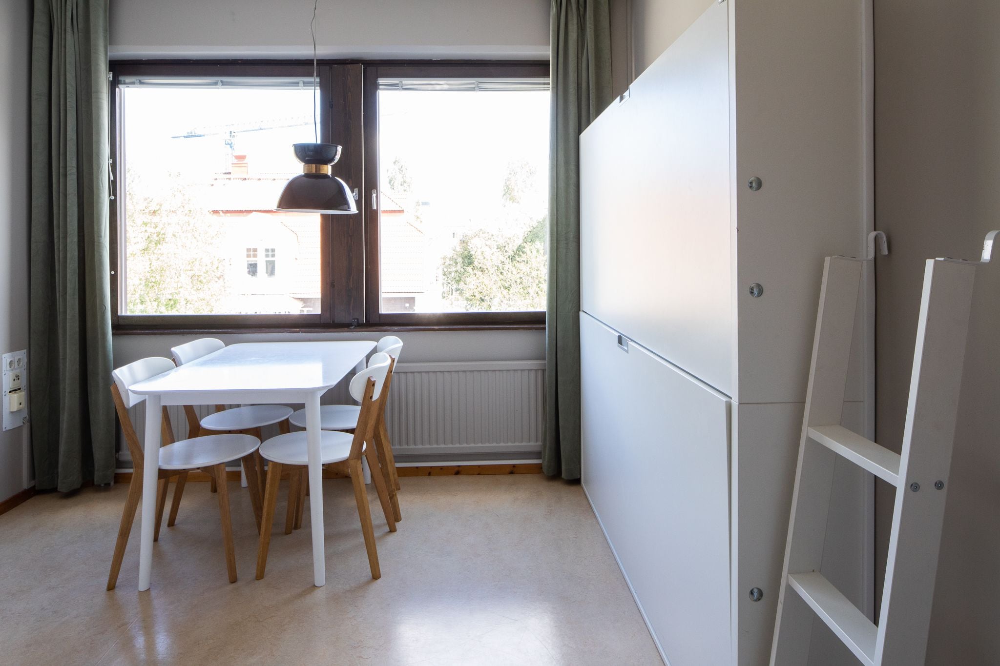 A room with a white table and chairs, a window with curtains, and a white cabinet.