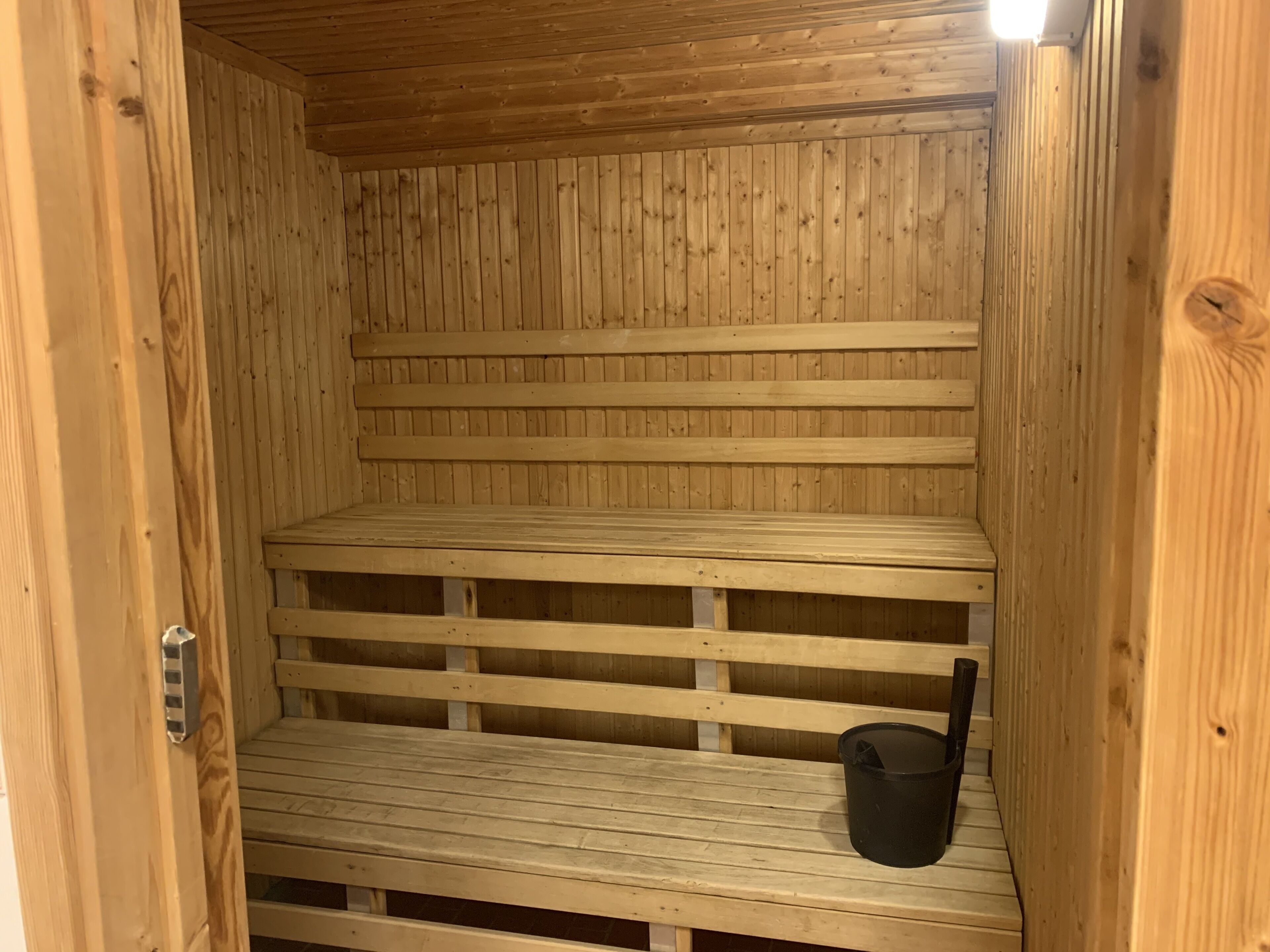 A wooden sauna with multiple benches and a black bucket.