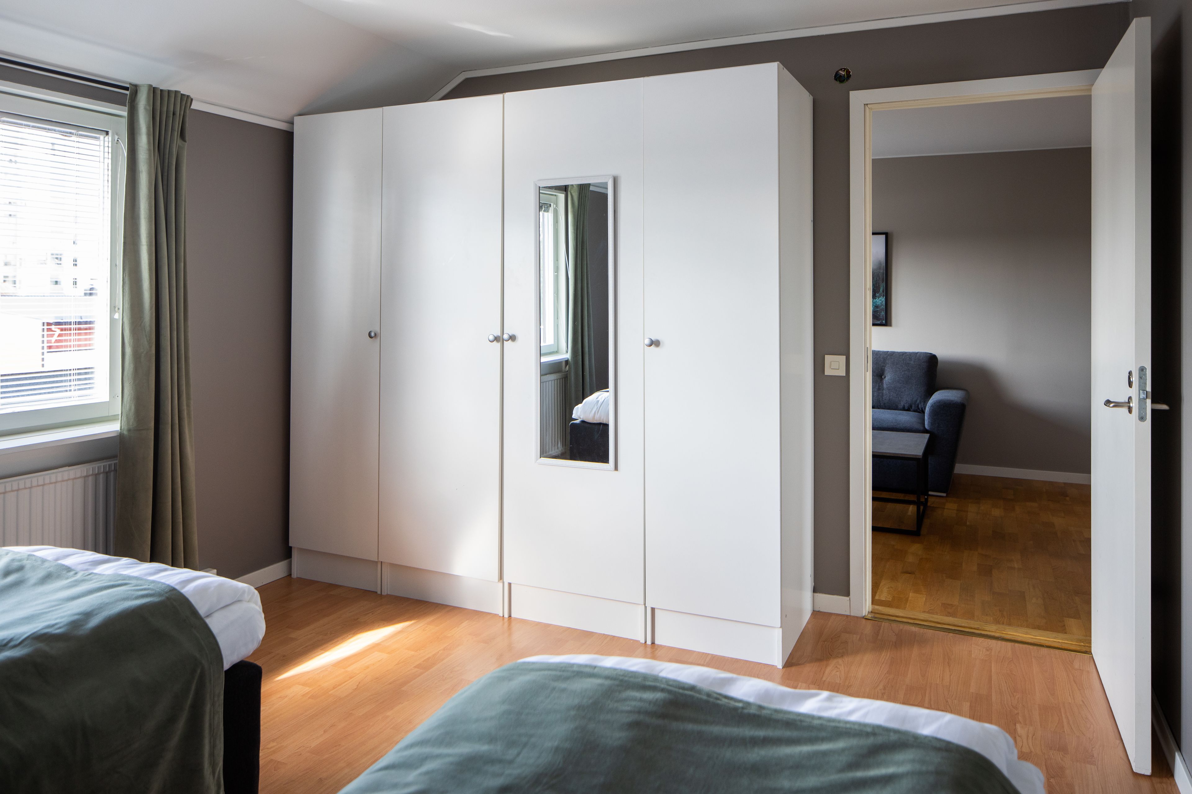 A bedroom with a large wardrobe, a bed, and a view of a cityscape through the window.