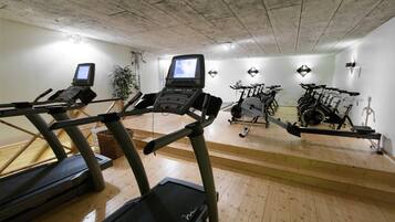 Een sportschool met loopbanden, hometrainers en een roeiapparaat.