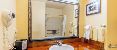Un baño con tocador de madera, un lavabo blanco, un espejo grande, un secador de pelo y un cuadro en la pared.