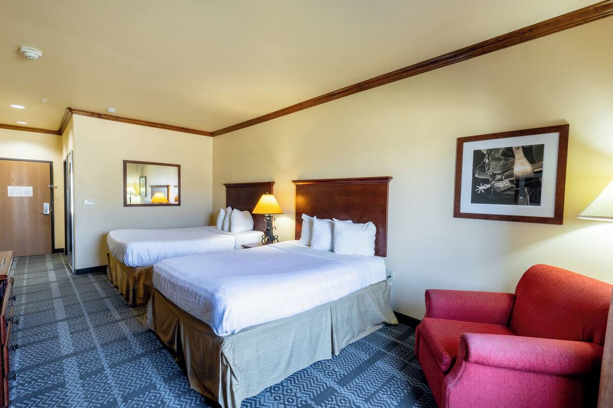 A hotel room with two beds, a red armchair, a framed picture on the wall, and a patterned carpet.