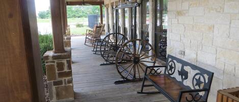 A covered porch with wooden flooring, stone walls, and a row of rocking chairs.