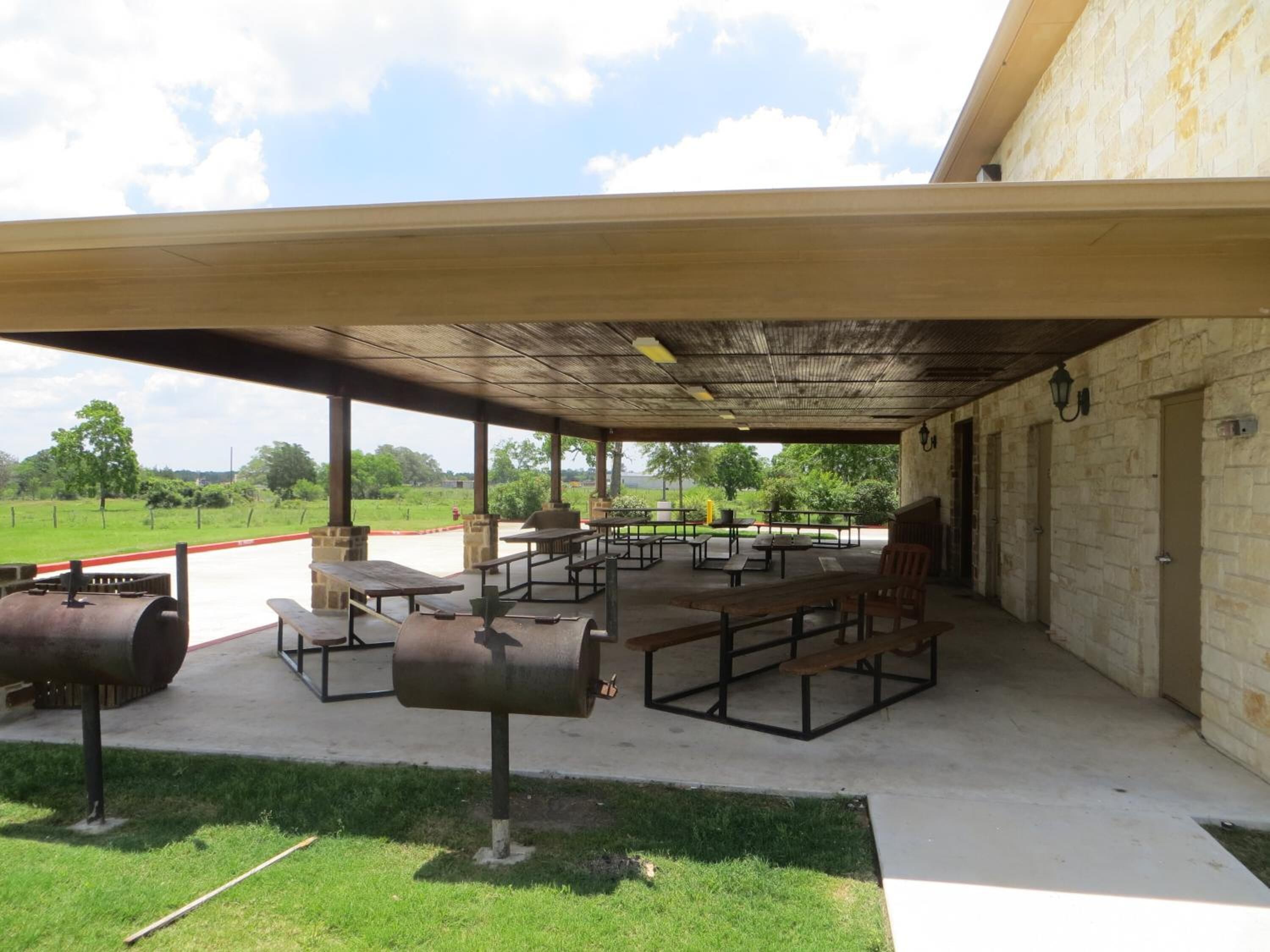 An outdoor covered patio with picnic tables and barbecue grills.