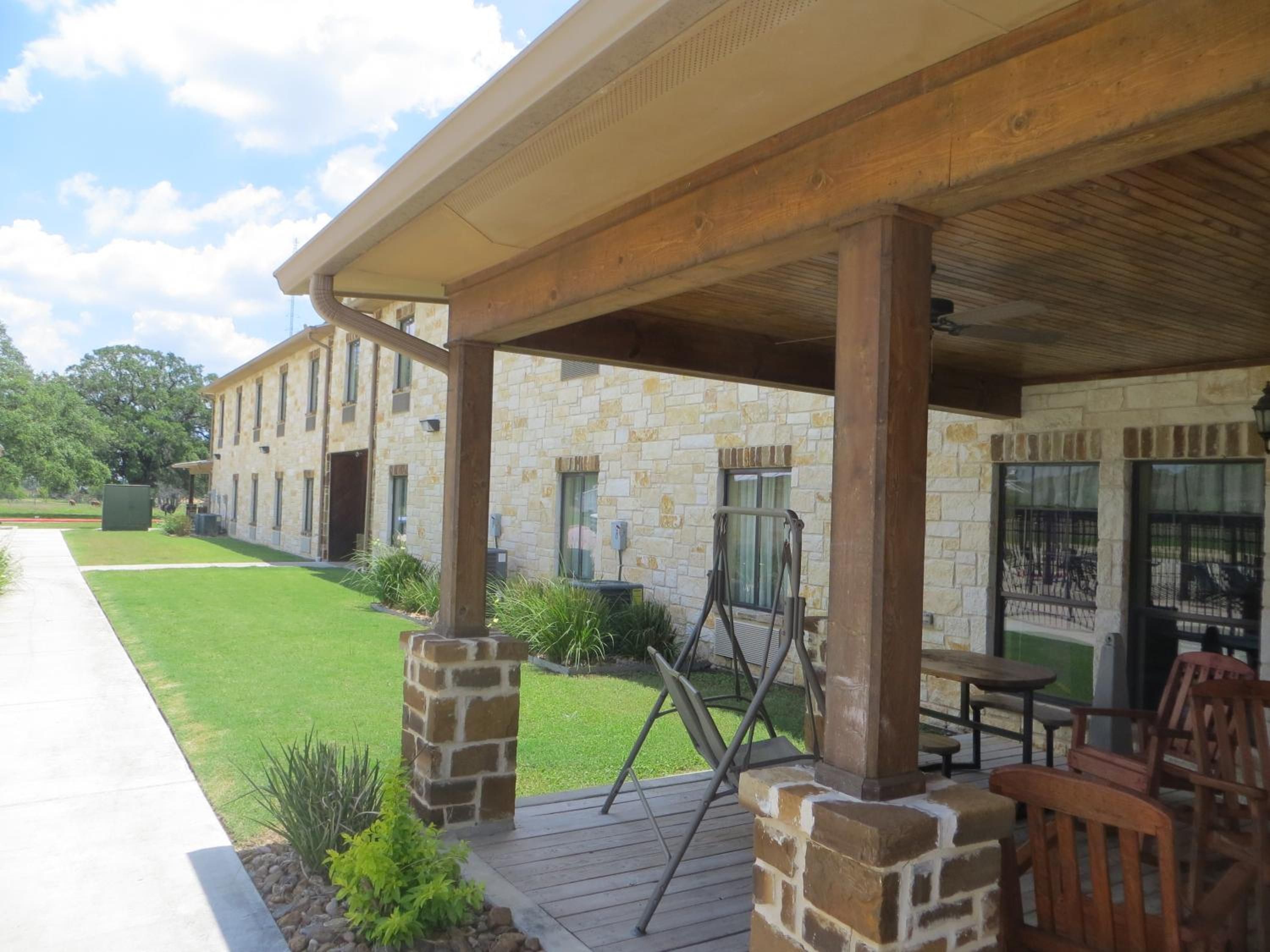 A covered patio area with stone pillars, a lawn, and a building in the background.