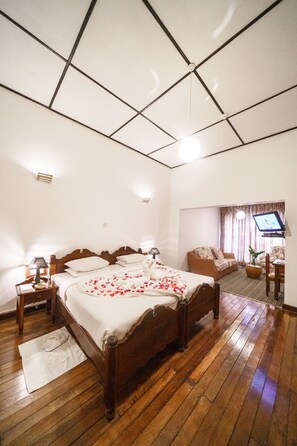 A bedroom with a wooden bed, a sofa, a television, and a small table. - Hotel Glendower (Nuwara Eliya)